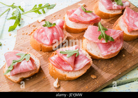 Foto von Baguette mit Schinken und Grüns auf weißer Holztisch Stockfoto