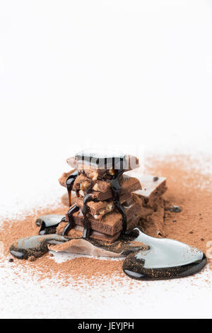 Stücke von Schokolade mit Kakao-Pulver, bestreut mit Sirup auf leeren weißen Hintergrund Stockfoto