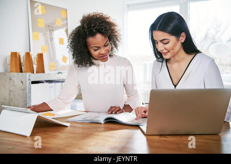 Zwei junge Frauen arbeiten zusammen in einem Büro an Ihrem Small Business lesen einen Bericht oder Papierkram mit zufrieden Lächeln Stockfoto