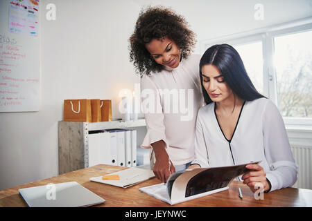 Zwei junge Frauen, die Führung eines kleinen Unternehmens arbeiten an Papierkram zusammen in das Büro Paging durch einen Bericht mit textfreiraum neben Stockfoto