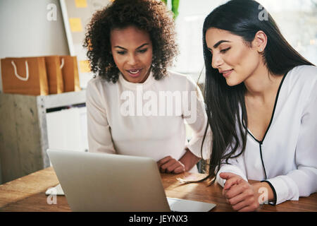 Zwei attraktive junge Frauen bei Arbeiten in einem Büro mit einer Diskussion, wie sie teilen sich einen Laptop zusammen lesen von Informationen auf dem Bildschirm Stockfoto