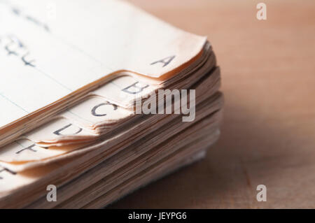 Nahaufnahme eines alten, Index im Registerkartenformat Adressbuchs mit vergilbten und furled Seiten, platziert auf einem Holztisch mit Licht, das von links aus Rahmen und einige Stockfoto