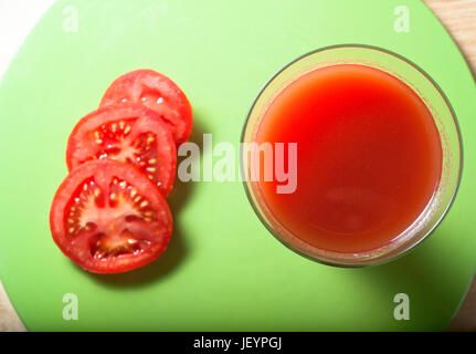Overhead Schuss von Tomatensaft in einem langen, hohen Glas neben drei Scheiben auf einer frischen grünen kreisrunde Matte, ruhen auf Birke Holz Tisch. Stockfoto