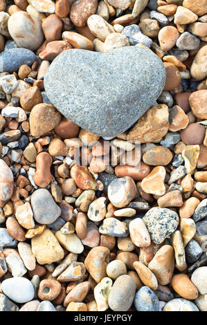 Eine graue herzförmige Stein im oberen Rahmen ruht auf einer Vielzahl von kleineren Steinen.  Im Hochformat (vertikal). Stockfoto