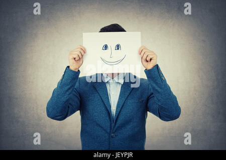 Geschäftsmann, bedeckte sein Gesicht mit ein Weißbuch mit gezeichneten lächelndes Emoticon-Skizze, wie eine gefälschte Maske zu verstecken seine echte Emotionen aus der Gesellschaft. Isola Stockfoto