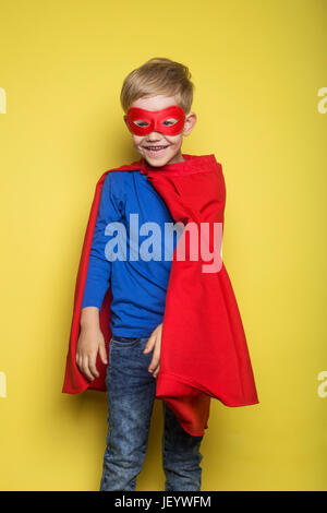 Junge im roten Superhelden Cape und Maske. Superman. Studio-Porträt auf gelbem Hintergrund Stockfoto