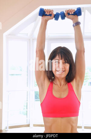 Lächelnde ältere Frau im Fitnessstudio trainieren. Ältere Frau heben die blaue Hanteln Stockfoto