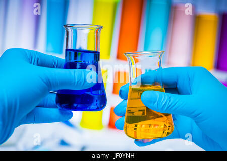 Techniker vergleicht zwei Fläschchen mit farbenfrohen Stoffen in einem Labor. Chemie und Wissenschaft Ausrüstung. Stockfoto