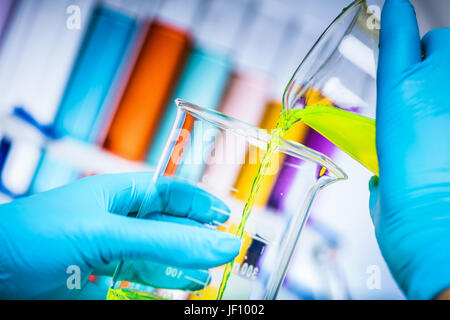 Wissenschaftler mischt zwei bunte Stoffe in einem Labor. Flüssiger, eine Kanne gießen. Chemie und Wissenschaft Ausrüstung. Stockfoto