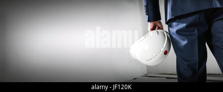 Geschäftsmann Holding weißen Schutzhelm. Weiße Betonwand. Wohnsiedlung und Bauindustrie. Banner-Format. Stockfoto