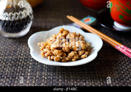 Eine Nahaufnahme von Natto (Japanisch fermentierte Bohnen) auf einem weißen Teller vor einem dunklen Hintergrund. Stockfoto