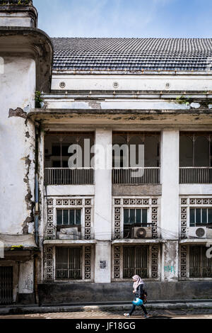 Lokale Frau zu Fuß vorbei an einer alten, verfallenen, weißes Gebäude in Semarang, Indonesien. Stockfoto