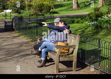 16. April 2017 - London, uk - eine nicht identifizierte junge Paar nimmt Selfie sitzen auf einer Bank im öffentlichen Park Stockfoto