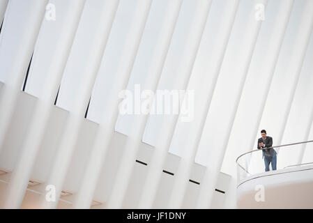 Eine Person, die allein in einem Atrium durch ein Geländer, unter einem hohen weißen zerfurcht Decke. Stockfoto