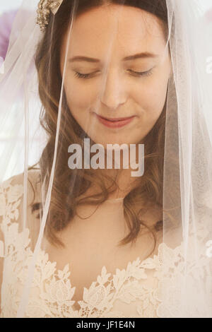 Eine junge Frau, eine Braut ein Hochzeitskleid mit Spitzen Mieder und einen Netto Schleier über das Gesicht. Stockfoto