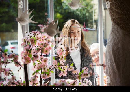 Zwei Frauen, eine junge Frau und eine reife Frau, die durch das Fenster auf ein Kleid auf dem Display in einer Braut Boutique suchen. Stockfoto