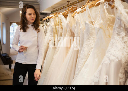 Reihen von Hochzeitskleider auf dem Display in einem Fachgeschäft Hochzeit Kleid. Eine Frau mit einem Glas Champagner, Blick auf ein Rack mit Couture-Kleider mit la Stockfoto