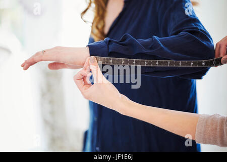 Eine Verkäuferin, Schneiderin oder Schneiderin, die Messungen eines Clients in einem Kleidungsgeschäft Hochzeit. Stockfoto