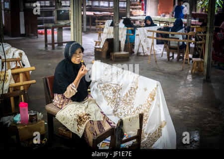 Mehrere Personen arbeiten in einem Batik-Workshop in Indonesien. Frau im Vordergrund wird Wachs auf das Design angewendet. Stockfoto