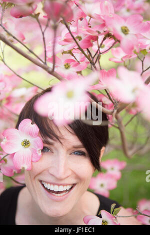 Eine Frau auf der Suche durch die blühenden Zweige eines Baumes und lächelnd. Stockfoto