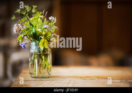 Nahaufnahme von Glas mit kleinen Haufen von wilden Blumen auf einem Holztisch. Stockfoto