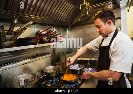 Koch in Küche, Stand trägt Schürze, kochen Suppe auf dem Herd mit Kelle rühren. Stockfoto