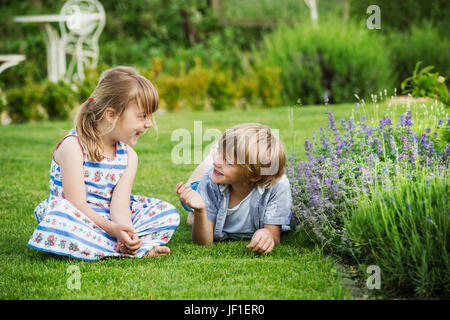 Ein Mädchen sitzt auf dem Rasen im Gespräch mit ihrem Bruder lag neben ihr auf dem Rasen im Garten. Stockfoto