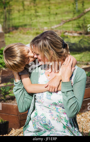 Mutter und Sohn, eine Frau sitzt auf einer Gartenbank ihres Sohnes auf die Wange küssen. Stockfoto
