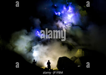 Silhouetten von zwei Wanderer eingehüllt in waberndem Rauch aus der faszinierenden Blauen Feuer des Ijen Krater, Indonesien. Stockfoto