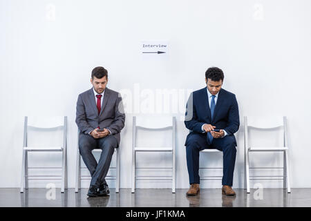 Geschäftsleute in Anzügen sitzen auf Stühlen im weißen Warteraum. Business-meeting Stockfoto