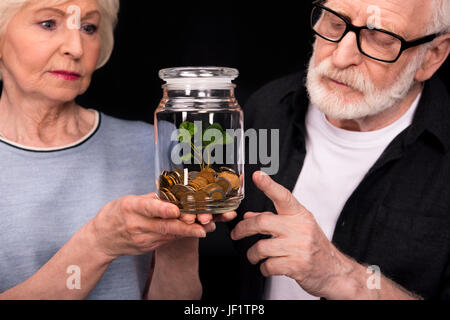 Nahaufnahme von älteres paar stehen zusammen und suchen bei Münzen und Pflanze in Glas Stockfoto