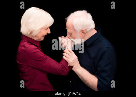 ältere Mann küssen Frauenhand isoliert auf schwarz, senior Paar glücklich Konzept Stockfoto