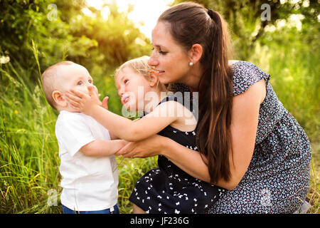 Schöne junge Mutter mit kleinen Kindern, die gemeinsame Zeit draußen im grünen Sommer Natur. Stockfoto