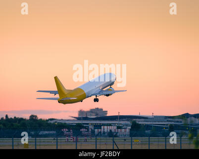Flugzeug abheben bei Sonnenuntergang von der Startbahn. Industrielandschaft mit Frachtflugzeug ist am Abend in den orangefarbenen Himmel fliegen. Schöne Luft frei Stockfoto