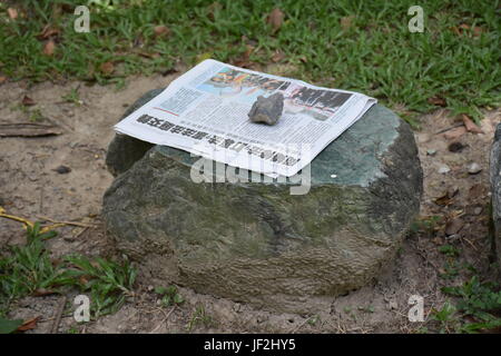 Stuhl aus Stein im Park auf dem Rasen mit Zeitung ruht auf Top und Rock gedrückt halten. Taiwan Stockfoto