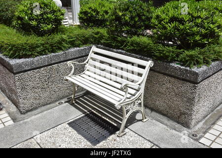 Weiße Bank mit antiken Stil im Gartenbereich neben Steinmauer in Gemeinschaft. Stockfoto