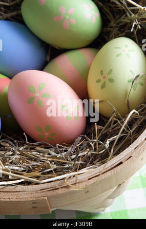 Nahaufnahme von bunten, von hand bemalte Ostereier eingebettet in Stroh in einem Korb auf einer karierten Tischdecke. Erschossen von oben. Stockfoto