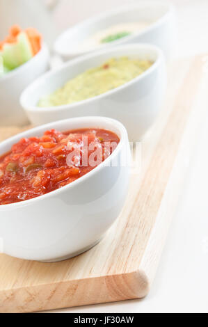 Nahaufnahme einer Schüssel Tomaten-Salsa, Guacamole, Hummus Dips und Crudites im Hintergrund. Stockfoto