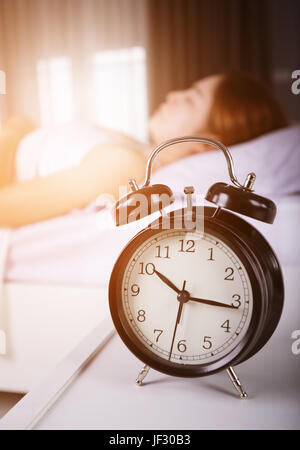 10:00 Uhr anzeigen und Frau schläft auf Bett mit Sonnenlicht am Morgen Stockfoto