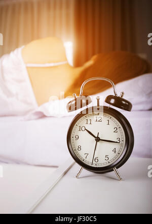 10:00 Uhr anzeigen und Frau schläft auf Bett mit Sonnenlicht am Morgen Stockfoto