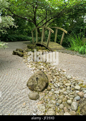 Japanische Zen Stil Garten geharkt Kies, verzierten hölzernen Brücke und Fluss Kiesel, Barnsdale Gärten, Rutland, England, UK. Stockfoto