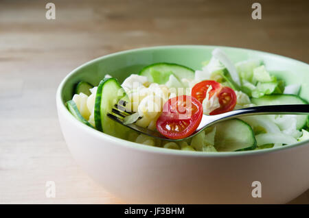 Fusili Nudeln mit Salat und Gabel in einer Schüssel auf einem Leuchttisch aus Holz. Stockfoto