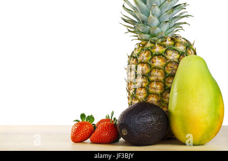 Eine Frucht-Komposition aus Ananas, Mango, Avocado und Erdbeeren auf einem hellen Holztisch vor einem weißen Hintergrund.  Kopieren Sie Raum nach links. Stockfoto