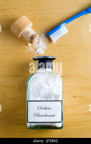 Eine Zahnbürste und eine Flasche von Natriumbicarbonat (Natron) flach und Schuss von oben auf einem Holztisch gelegt.  Cork öffnen und Pulver Verschütten auf t Stockfoto