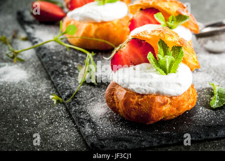 Sommer Desserts. Homemade backen. Kuchen Windbeutel mit Sahne, frische Erdbeeren, Minze und Prise Puderzucker. Auf einem schwarzen Stein ta Stockfoto