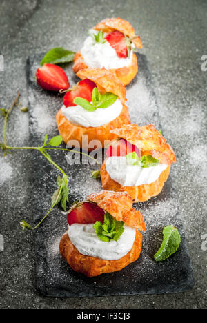 Sommer Desserts. Homemade backen. Kuchen Windbeutel mit Sahne, frische Erdbeeren, Minze und Prise Puderzucker. Auf einem schwarzen Stein ta Stockfoto