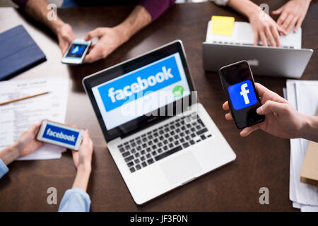 Schuss von Geschäftsleuten mit digitalen Geräten mit Facebook Logo Symbole auf Bildschirmen abgeschnitten Stockfoto