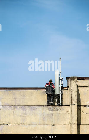 Ein Arbeiter Festsetzung einer Mobilfunk-Antenne auf dem Dach des Gebäudes. Blauer Himmelshintergrund Stockfoto