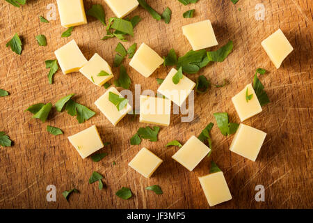 Würfel von gelben Käse mit Kräutern nach dem Zufallsprinzip auf Schneidbrett aus Holz gestapelt Stockfoto