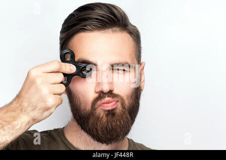 Junger Mann hält und spielt mit Fidget Spinner. Studio auf weißem Hintergrund gedreht. Stockfoto